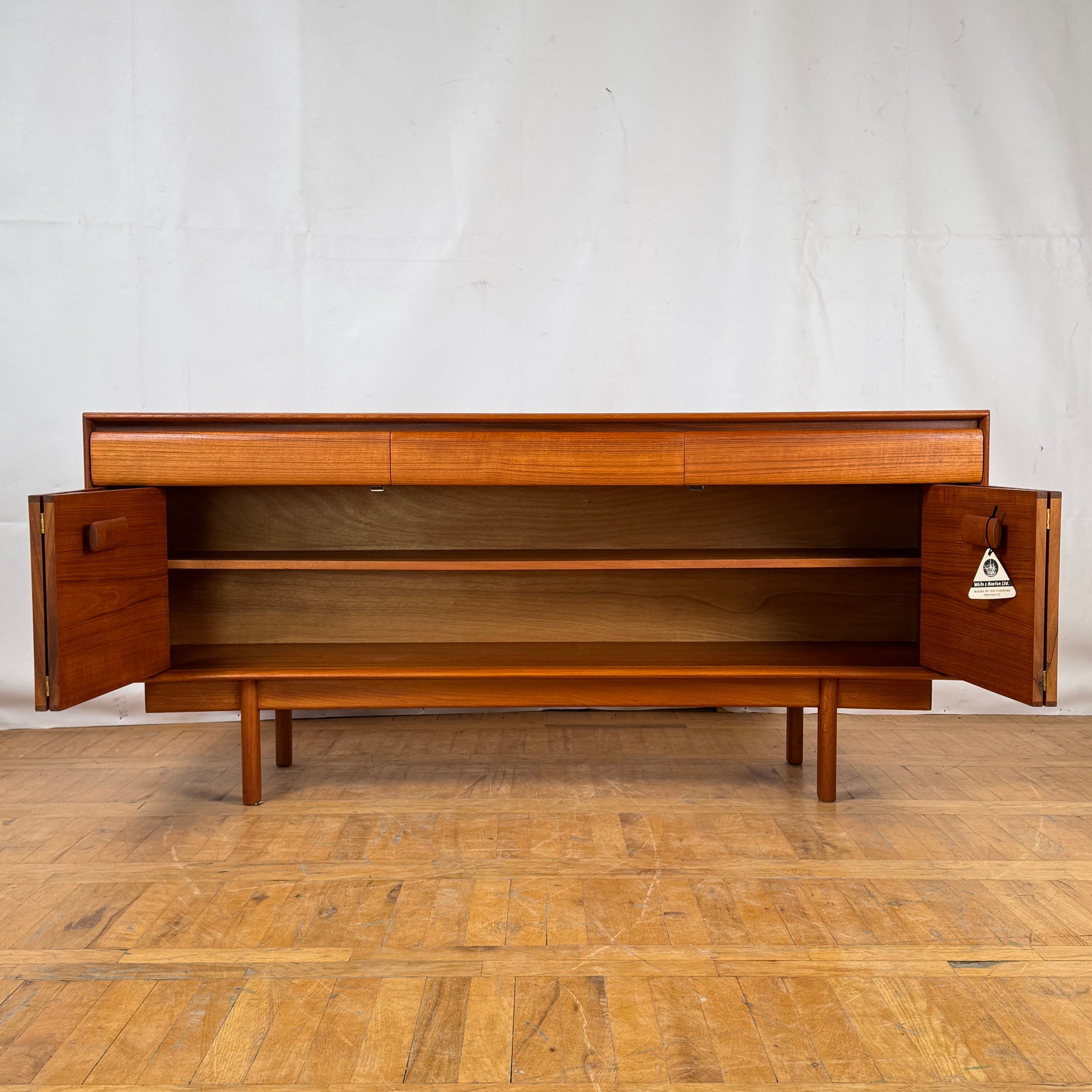 Wooden sideboard with open doors on a wooden floor against a white wall